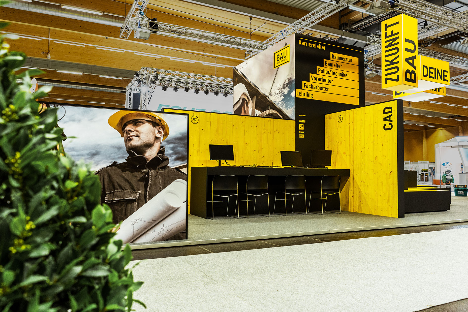 Messestand der BauAkademie mit gelber Wandgestaltung, schwarzen Thekenelementen und Präsentationsflächen