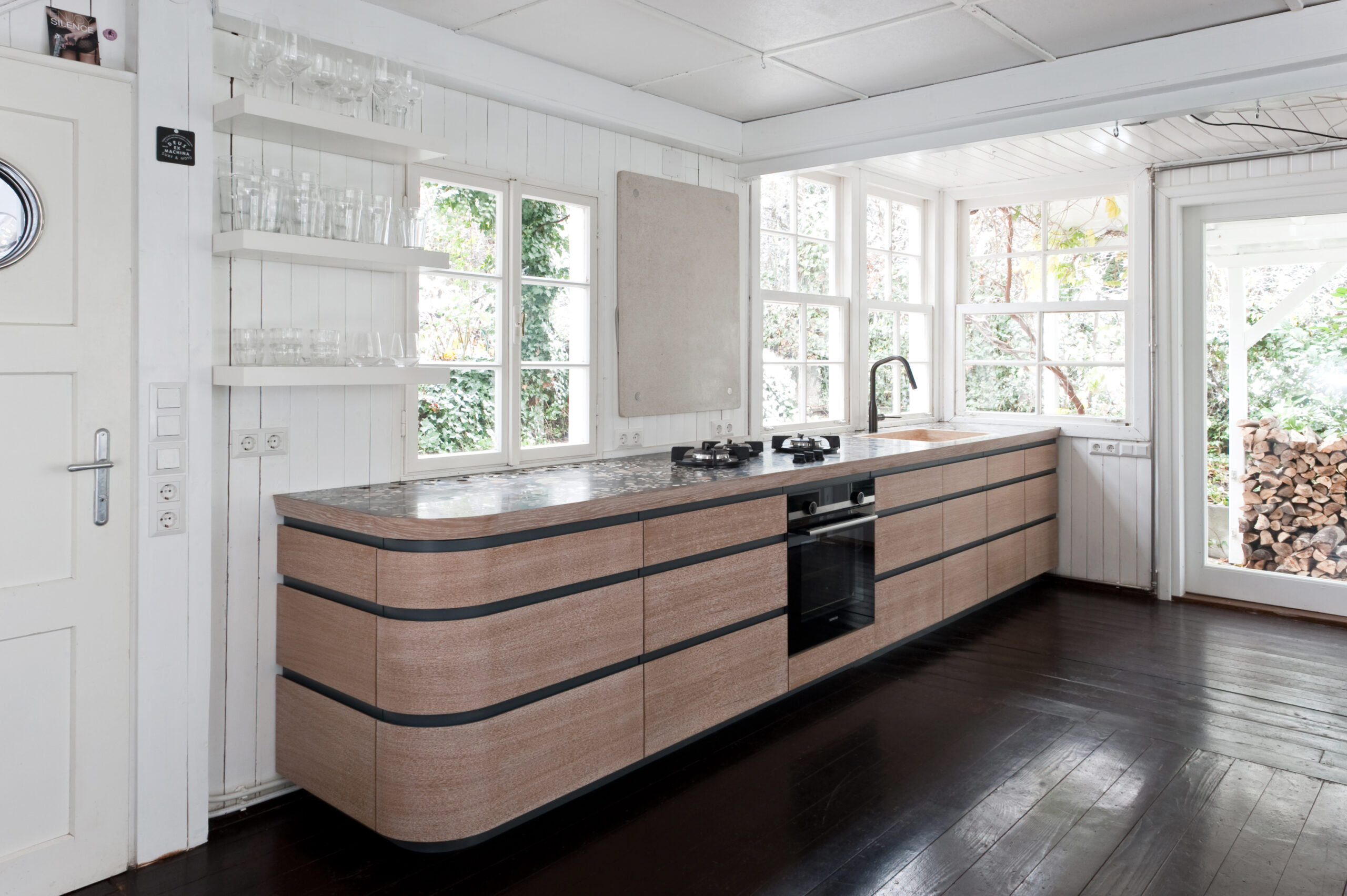 Moderne Küche mit gebogener Holzinsel und heller Fensterfront im Projekt The Snake House Kitchen