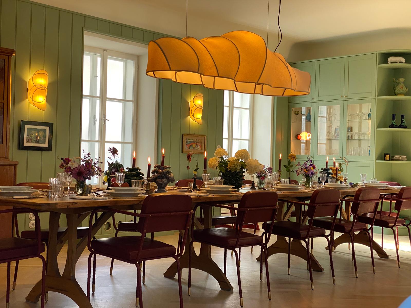 Esszimmer mit langer Tafel, orangefarbenen Pendelleuchten und grünen Wänden